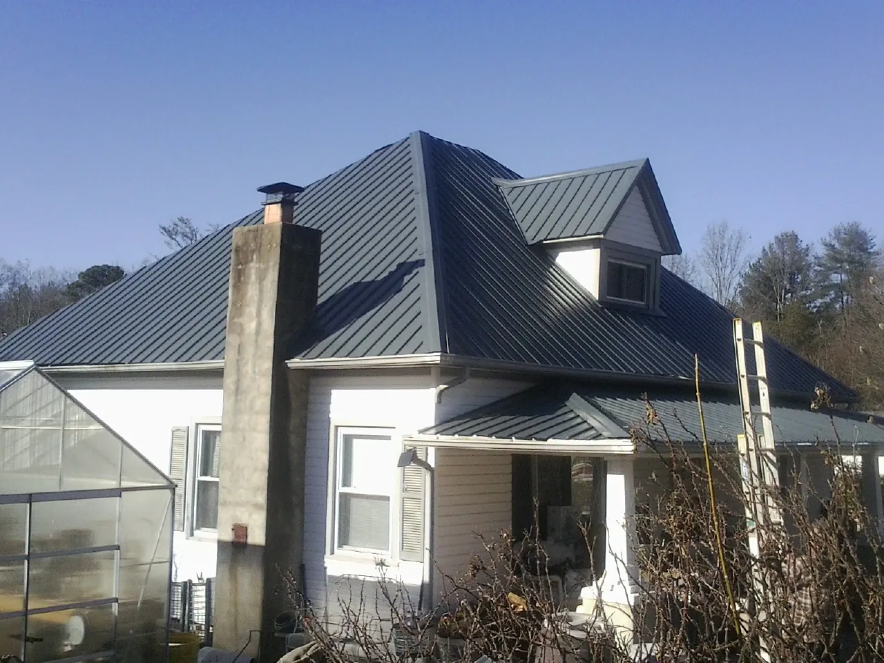 Dark blue standing seam metal roof on a white farmhouse with dormer — Slate & Tile Roof Repair by Roofing Brothers in Hialeah