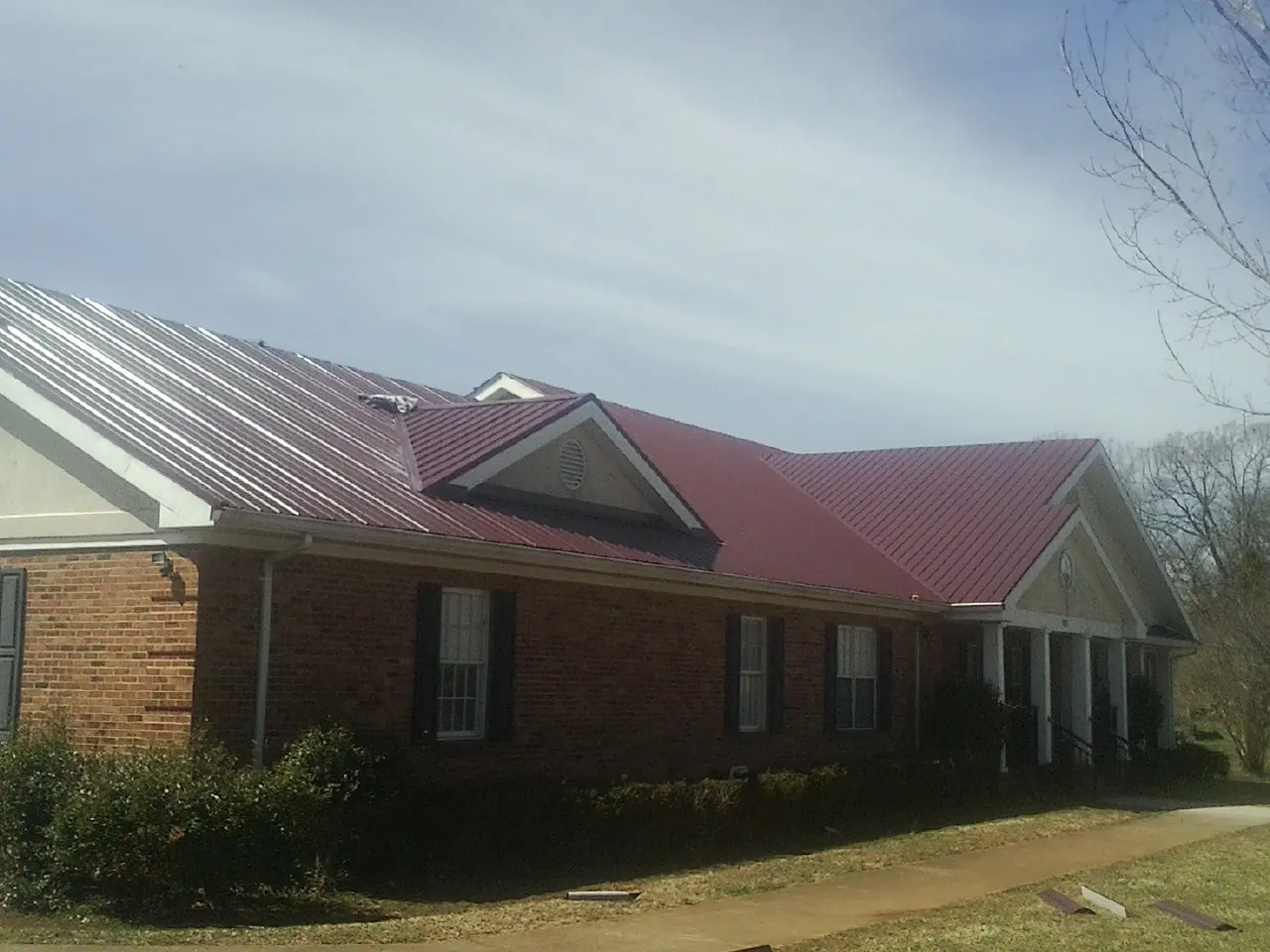 Red metal roof with gabled entries on a long brick building, from a Hail Damage Roof Repair job in Hialeah