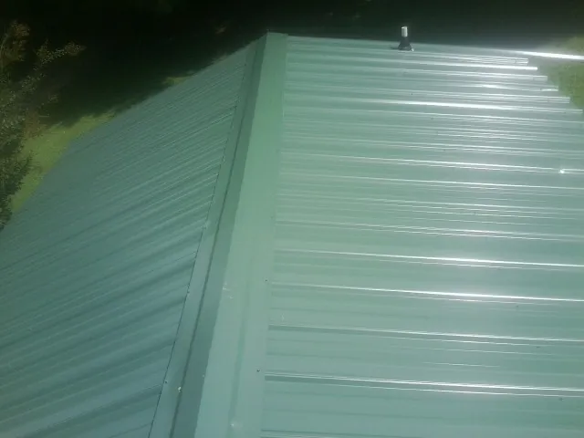 New green metal panels meeting at the ridge of a roof — Flat Roof Repair work by our crew in Hialeah