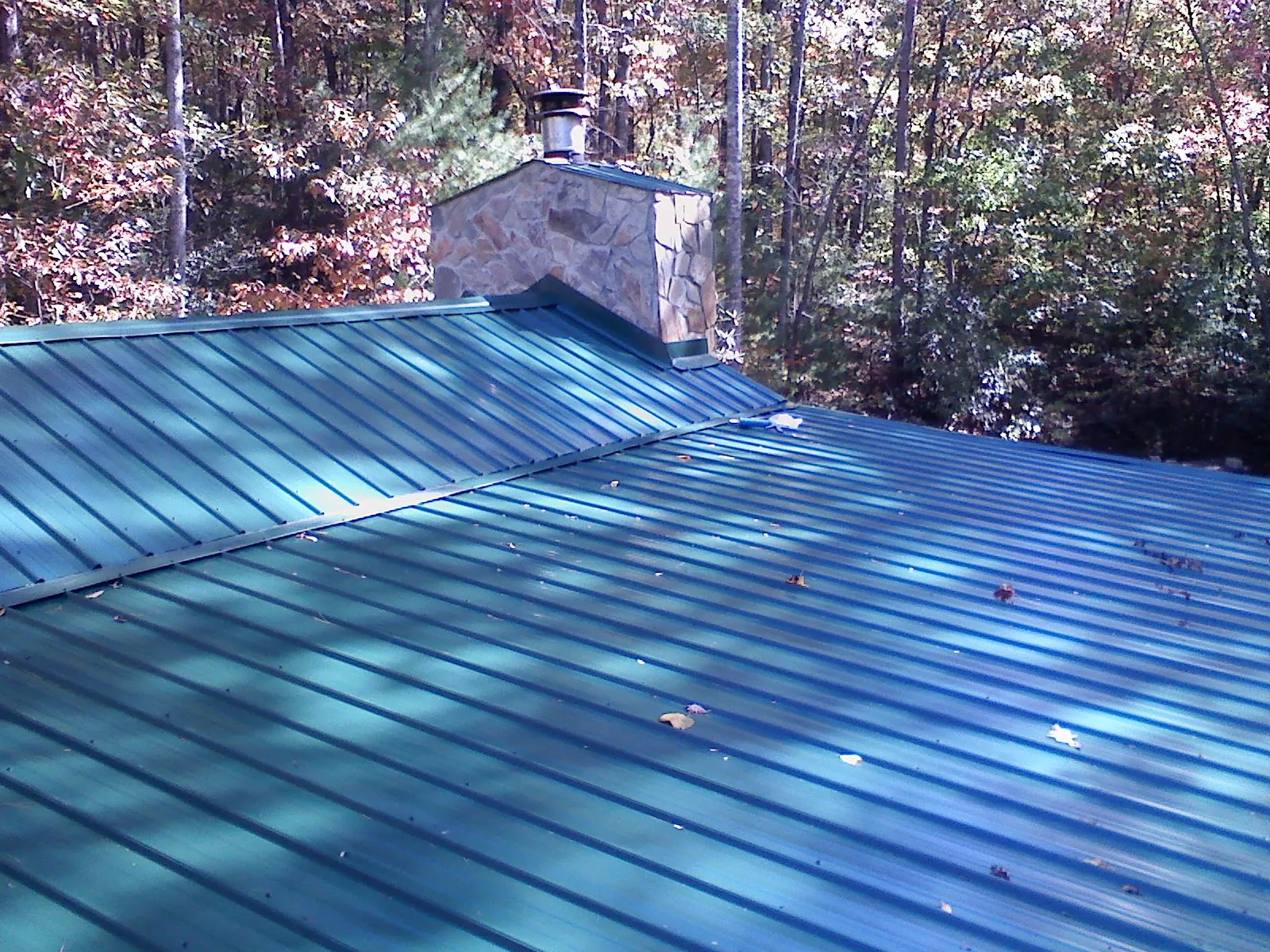 New green metal roof and stone chimney surrounded by autumn woods in Hialeah