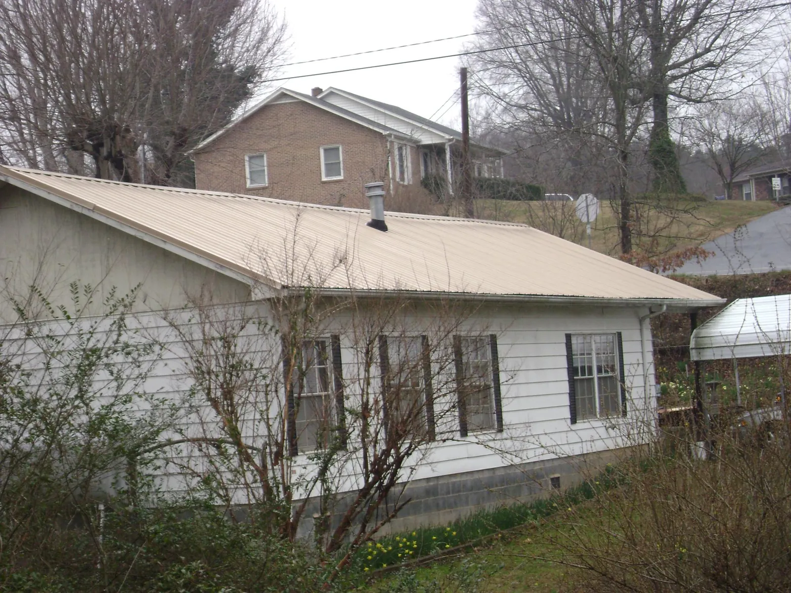 Tan metal roof on a white sided house set into a hillside — Commercial Roofing by Roofing Brothers in Hialeah